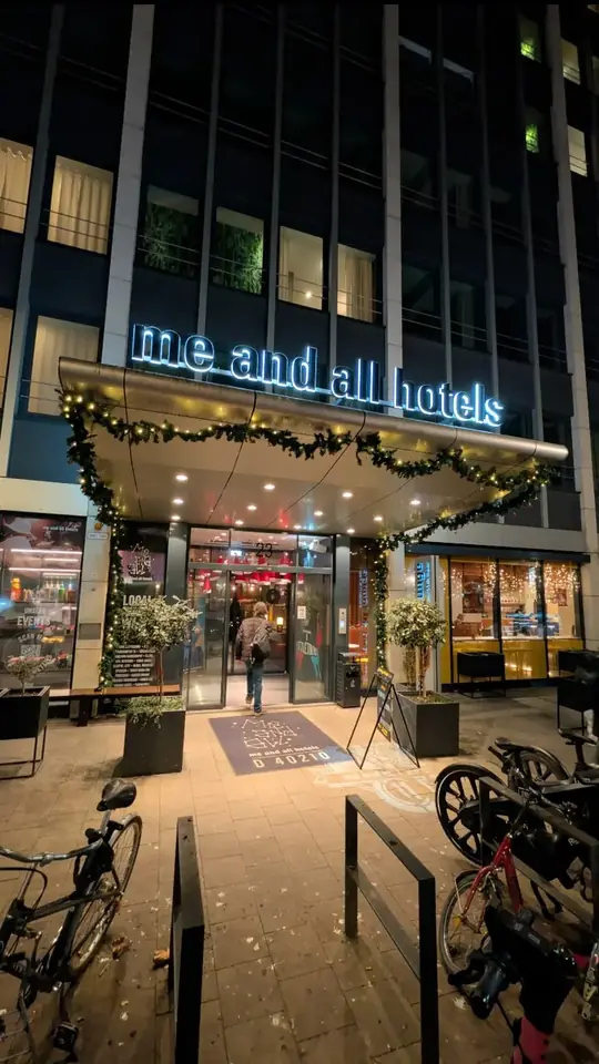 Cover: Eingang des Me and All Hotels in Düsseldorf am Abend, mit Lichterketten.